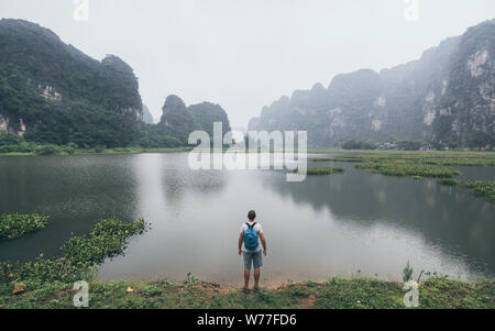 Caucasian man surplombant les montagnes de calcaire dans la province de Ninh Binh, Vietnam. Journée nuageuse, la réflexion dans l'eau Banque D'Images