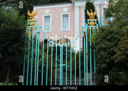 Image d'une petite porte bleue avec des oiseaux d'or detailings à côté de quelques buissons, en face d'un bâtiment, sur une journée ensoleillée à Portmeirion Banque D'Images