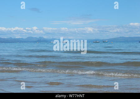 Droit de la mer calme, avec des montagnes et des petits nuages dans la distance, sur une journée ensoleillée à Abersoch Banque D'Images