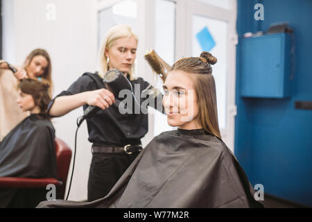 Portrait de femme heureuse au salon de coiffure. Coiffure professionnel concept. Coiffure cheveux longs fille de séchage en utilisant un sèche-cheveux et d'un pinceau. Avec le séchage Banque D'Images