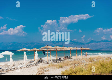 Plage de sable avec beaucoup de chaises longues, parasols en paille, avec des vagues de la mer bleu-vert magnifique, ciel bleu avec de petits nuages blancs et des montagnes majestueuses. Conce Banque D'Images