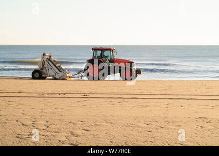 BALAYAGE matinal : un tracteur avec un dispositif de sifting attaché nettoie et élimine les déchets de la plage de Virginie dans les premières heures de l'aube. Banque D'Images