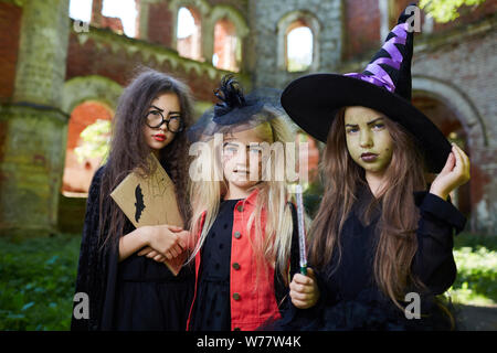 Taille portrait de trois petites sorcières looking at camera tout en se posant en spooky castle sur Halloween, copy space Banque D'Images