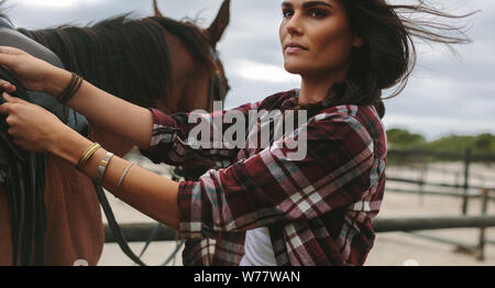 Les jeunes d'une selle fixation cowgirl brun sur un cheval avant l'équitation. Femme cheval Cavalier obtenir prêt à monter. Banque D'Images