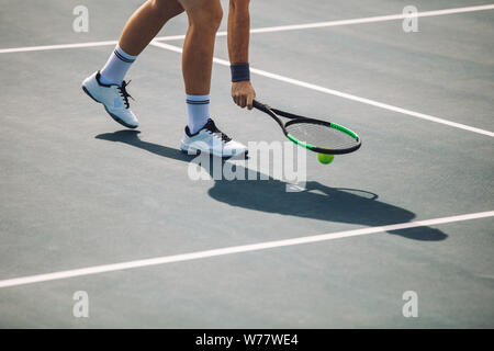 Cropped shot de sportif sur tennis picking la balle avec la raquette. Joueur de tennis masculin ramasser la balle sur surface dure. Banque D'Images