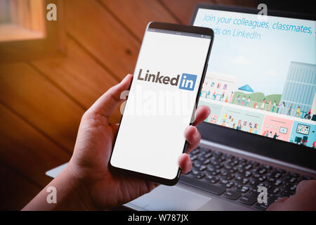 Bangkok, Thaïlande - 5 août 2019 : Hands holding Smartphone avec LinkedIn logo sur écran et site web de LinkedIn sur fond d'ordinateur portable. Linkedin est un po Banque D'Images