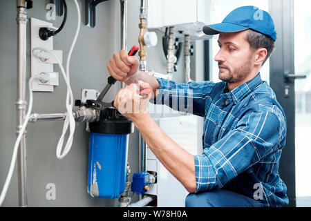 Jeune technicien plombier ou installation ou réparation de système de filtration de l'eau Banque D'Images