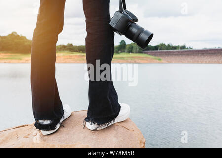 Photographe debout sur un rocher et tenant une caméra. Femme debout sur la roche près de la rivière. Banque D'Images