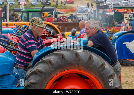 Deux vieux messieurs les agriculteurs ou les amateurs de tracteur ou de parler le chat s'appuyant sur un vieux millésime le tracteur à un pays. Banque D'Images