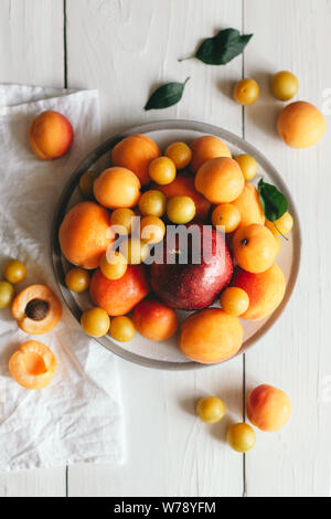 Pomme mûre, abricots et prunes-cerises sur une plaque blanche. Vue de dessus sur une table en bois. Banque D'Images