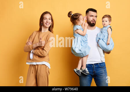 Malheureux papa fatigué de passer du temps avec les enfants, tandis que son épouse détendue heureux showing thumb up, ayant un reste. la fatigue et l'épuisement après Banque D'Images