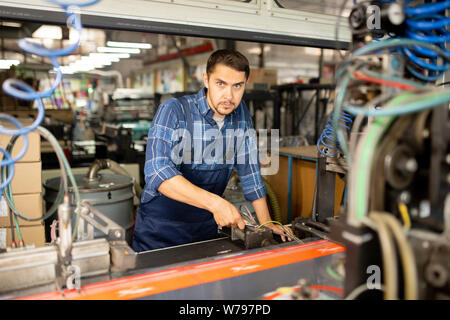 Jeune mécanicien ou technicien d'usine de travailler avec l'un des machines industrielles Banque D'Images