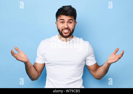 Je ne sais pas. close up portrait of confusion perplexe beau jeune homme barbu en t-shirt blanc debout avec les bras levés , open palms, isolé sur bl Banque D'Images