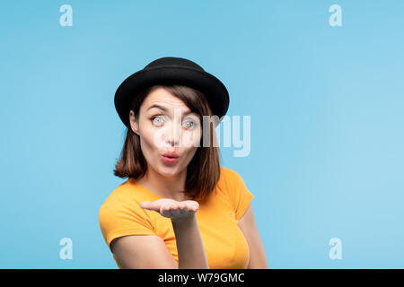 Flirty fille brune en noir hat vous envoyer kiss air Banque D'Images