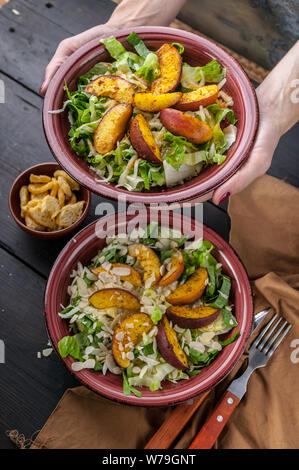 Close-up femme mains tiennent une assiette avec la salade végétalienne avec poêlée de pêche. Shot verticale Banque D'Images