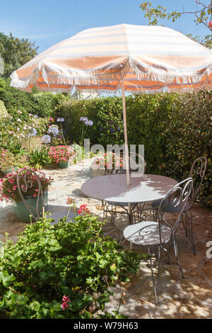 Terrasse fleurie avec mobilier de jardin en fer forgé et parasol Banque D'Images