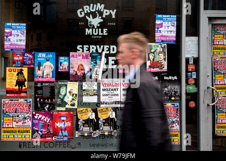 Un jeune homme marchant par affiches publicitaires pour Edinburgh Fringe Festival montre sur la fenêtre d'un café vide à Édimbourg, Écosse, Royaume-Uni. Banque D'Images