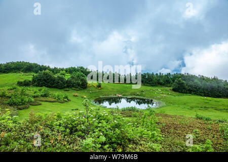 Vue d'une clairière de montagne avec un lac miroir transparent et de hautes montagnes avec des sommets enneigés au loin. Caucase, Russie Banque D'Images