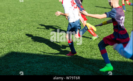 Les garçons en rouge et bleu joue au football sur terrain de sport, dribbles ballon. Les jeunes joueurs de soccer avec boule sur l'herbe verte. La formation, football Banque D'Images