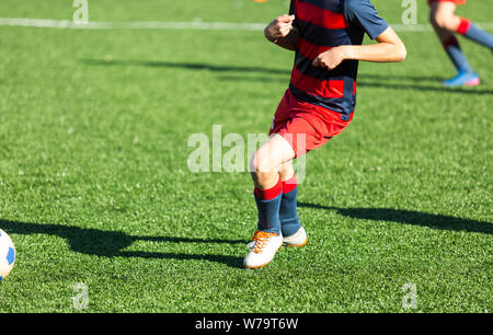 Les garçons en rouge et bleu joue au football sur terrain de sport, dribbles ballon. Les jeunes joueurs de soccer avec boule sur l'herbe verte. La formation, football Banque D'Images