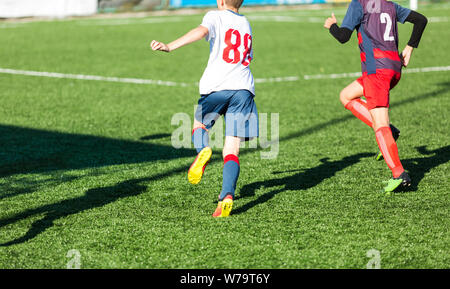 Les garçons en rouge et bleu joue au football sur terrain de sport, dribbles ballon. Les jeunes joueurs de soccer avec boule sur l'herbe verte. La formation, football Banque D'Images