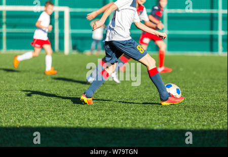 Les garçons en rouge et bleu joue au football sur terrain de sport, dribbles ballon. Les jeunes joueurs de soccer avec boule sur l'herbe verte. La formation, football Banque D'Images