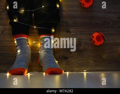 Les enfants dans les jambes chaudes élégante à rayures colorées lumineuses funny chaussettes dans Garland phares sur marbre avec des citrouilles en prix. décoration pour Halloween, chaleureux. Banque D'Images