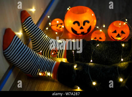 Les enfants dans les jambes chaudes élégante à rayures colorées lumineuses funny chaussettes dans Garland phares sur marbre avec des citrouilles en prix. décoration pour Halloween, chaleureux. Banque D'Images