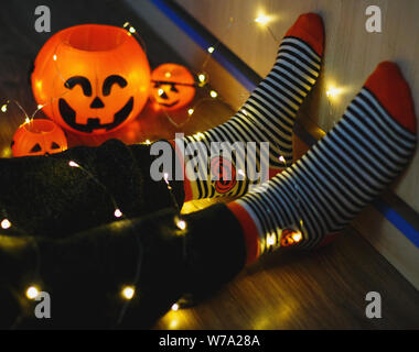 Les enfants dans les jambes chaudes élégante à rayures colorées lumineuses funny chaussettes dans Garland phares sur marbre avec des citrouilles en prix. décoration pour Halloween, chaleureux. Banque D'Images