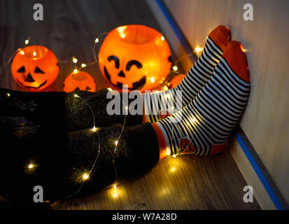 Les enfants dans les jambes chaudes élégante à rayures colorées lumineuses funny chaussettes dans Garland phares sur marbre avec des citrouilles en prix. décoration pour Halloween, chaleureux. Banque D'Images