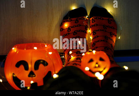 Les enfants dans les jambes chaudes élégante à rayures colorées lumineuses funny chaussettes dans Garland phares sur marbre avec des citrouilles en prix. décoration pour Halloween, chaleureux. Banque D'Images