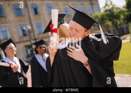 Deux diplômés hugging en face de leur université. Banque D'Images