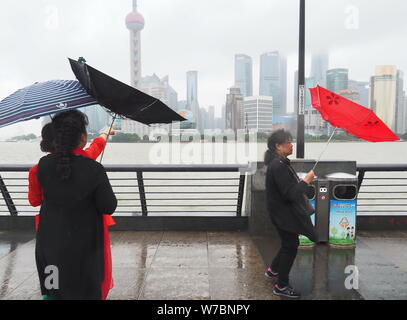 Les piétons tentent de se protéger avec des parasols contre le vent et les fortes pluies causées par le typhon Khanun sur le Bund le long de la rivière Huangpu dans Banque D'Images