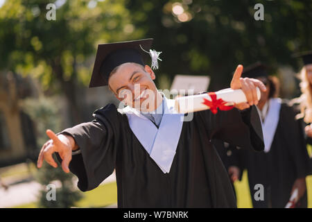 Garçon joyeux montrant tout le monde dans la cour de son diplôme. Banque D'Images