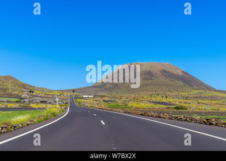 L'Espagne, Lanzarote, debout vis route à travers champs verts à mont volcanique volcan monte corona Banque D'Images