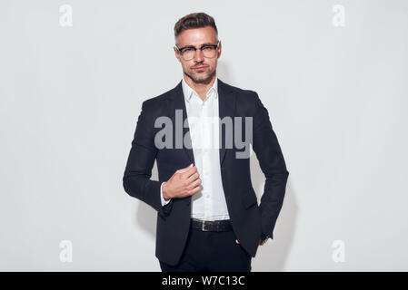 Look assuré. Portrait d'un homme d'affaires élégant en costume classique et veste de réglage de lunettes tout en se tenant sur fond gris. Beauté hommes. Aspect professionnel. Réussite Banque D'Images