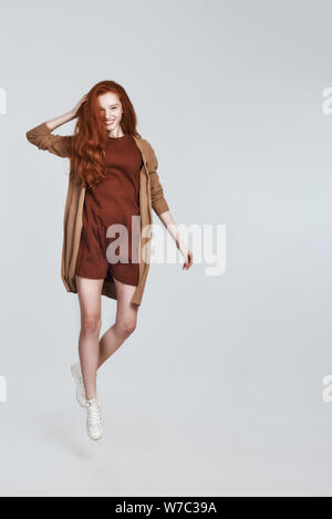 Studio shot of playful young woman with red hair smiling ébouriffés tout en sautant à l'arrière-plan gris. Concept de beauté. Le bonheur Banque D'Images