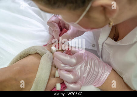 Au cours d'un maître de la pédicure. Le processus de la pédicure professionnelle. L'assistant dans le masque entraîne le gel de corail aux ongles avec une brosse. Le concept de Banque D'Images