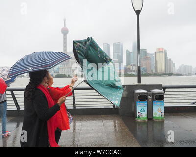 Les piétons tentent de se protéger avec des parasols contre le vent et les fortes pluies causées par le typhon Khanun sur le Bund le long de la rivière Huangpu dans Banque D'Images
