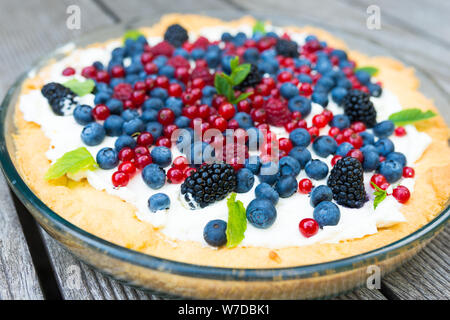 Tarte aux bleuets frais, framboises, mûres, groseilles rouges et crème fouettée décoré de feuilles de menthe. Vue de dessus Banque D'Images