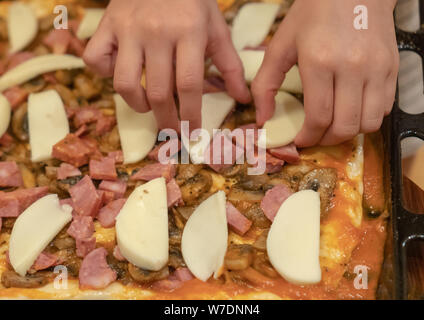 La fille de cuisiniers de la pizza. Mains de l'enfant les tranches de fromage mozzarella sur une pizza. Banque D'Images