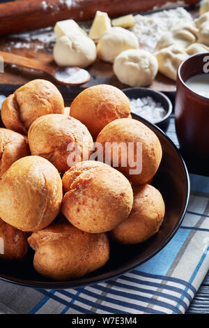 Close-up of Jamaican boulettes frites dans un bol noir sur une table en bois avec des ingrédients sur une planche en bois, vue verticale d'en haut, macro Banque D'Images