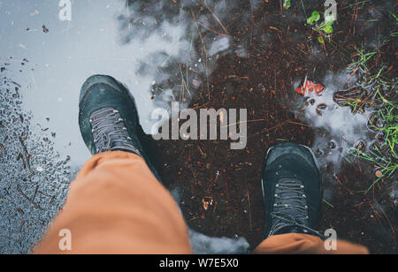 Homme staingg au cours automne pluvieux météo dans une flaque d'eau dans un imperméable chaussures de suivi. Météo automne Concept. Toute la saison adventure concept. Muddy backgrou Banque D'Images