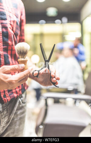 Close up de la mode de coiffure holding scissors et pinceau pour raser la barbe. Banque D'Images