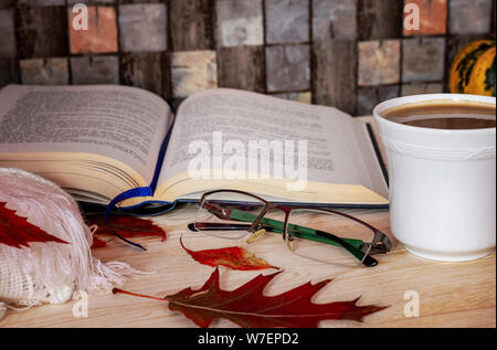 Style scandinave hygge. Livre ouvert avec tasse de café, blanc écharpe en tricot et feuilles d'automne sur la table en bois avec checkered background. Banque D'Images