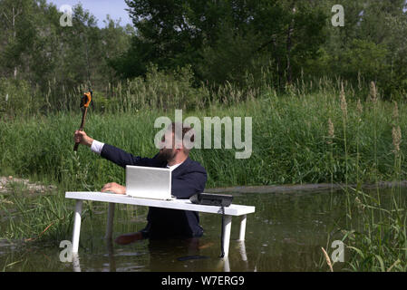 Jeune hipster barbu, au flanc, avoir du plaisir au travail et prendre un. selfies À la table, debout dans le marais, dans l'eau Banque D'Images