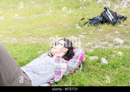 Voyages et loisirs concept, vacances, week-end. Woman traveler avec des lunettes de soleil allongés sur l'herbe et de détente dans les montagnes. Hipster girl resting, s Banque D'Images