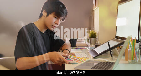 Jeune photographe professionnel travaillant sur ses images d'échantillons de couleur dans son bureau moderne Banque D'Images