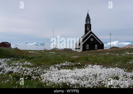 L'église de Sion à Ilulissat, Groenland, entourée de fleurs et d'icebergs de la baie de Disko en arrière-plan. Banque D'Images