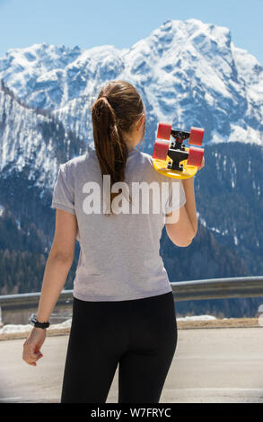 Une jeune femme aux cheveux blonds tenant une planche à roulettes et à la recherche sur les montagnes Banque D'Images